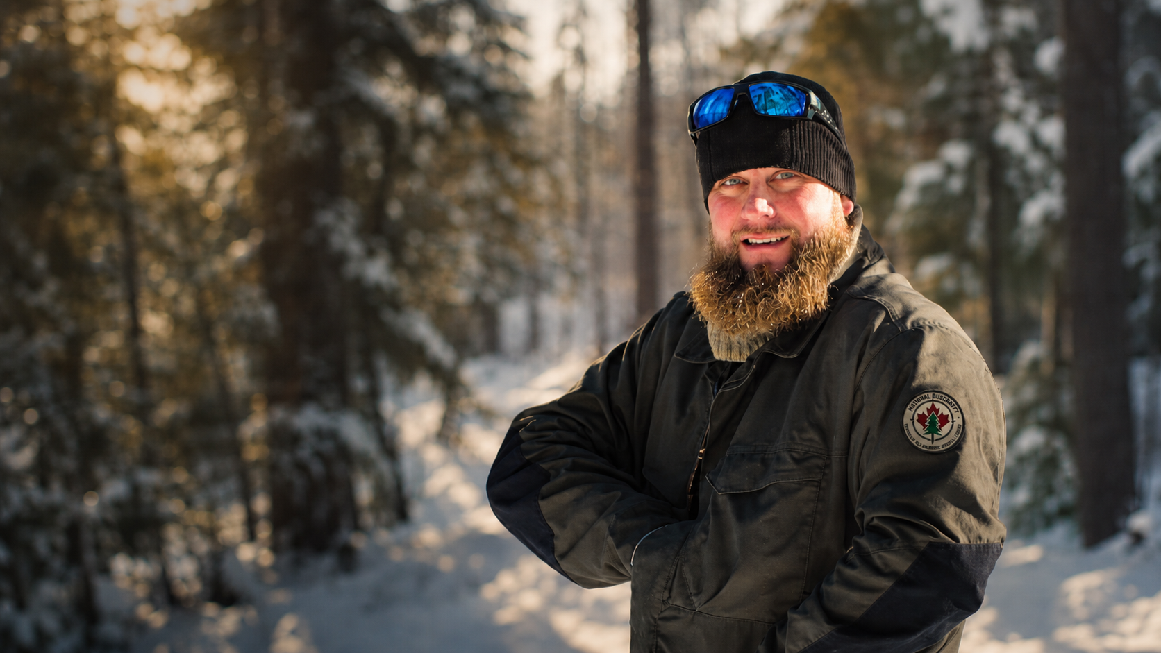 An NBSC instructor in winter gear standing in a snowy boreal forest